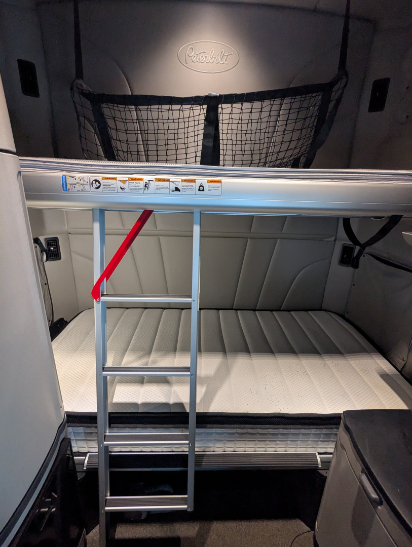 Peterbilt 579 sleeper cab interior cargo area with ladder and netting, storage space visible, cab paneling, and upper window area.