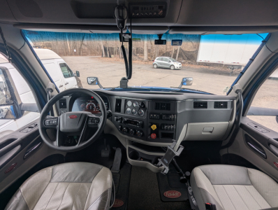 Peterbilt 579 truck cab interior dashboard and steering wheel view showing instrument cluster, central control panel, gear shifter, and seats.
