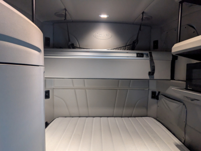Peterbilt interior sleeper cab with bunk area and overhead storage. The Peterbilt logo is visible in the curved cabinet panel above.