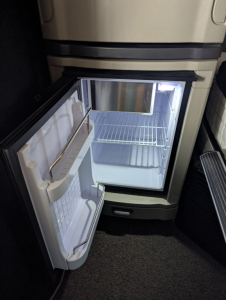 Refrigerator open in cab of a 2024 Peterbilt 579 truck showing empty freezer and two-door fridge with shelves.