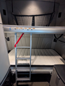 Peterbilt 579 sleeper cab interior cargo area with ladder and netting, storage space visible, cab paneling, and upper window area.