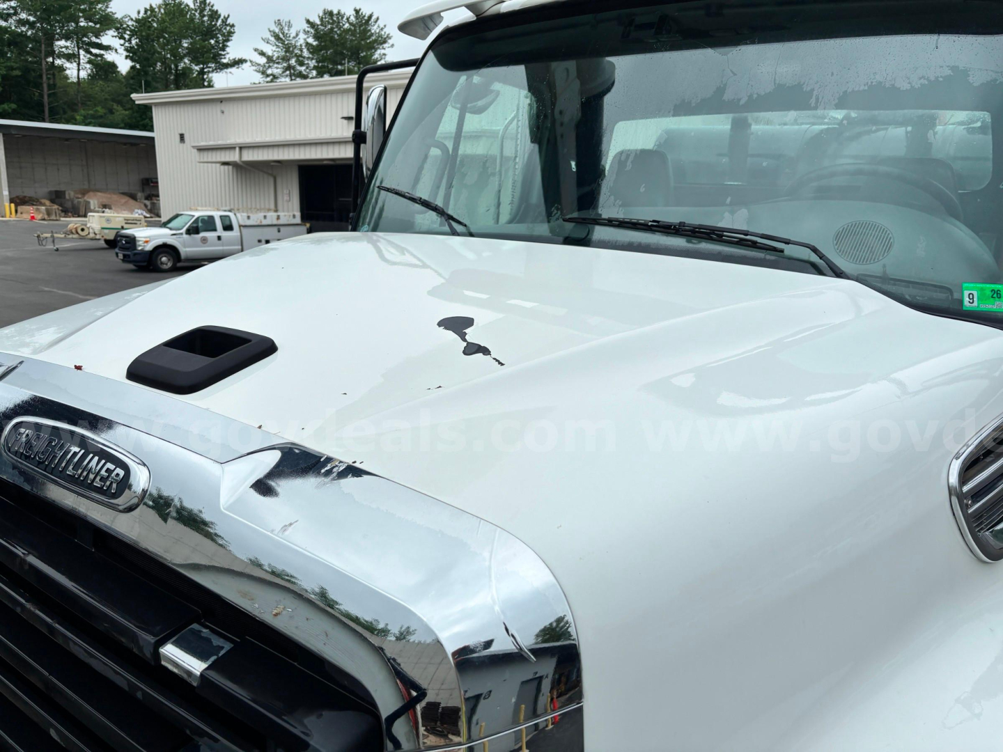 Front view of a 2013 Freightliner 114SD hood and windshield with a damaged hood and chrome grille area visible.