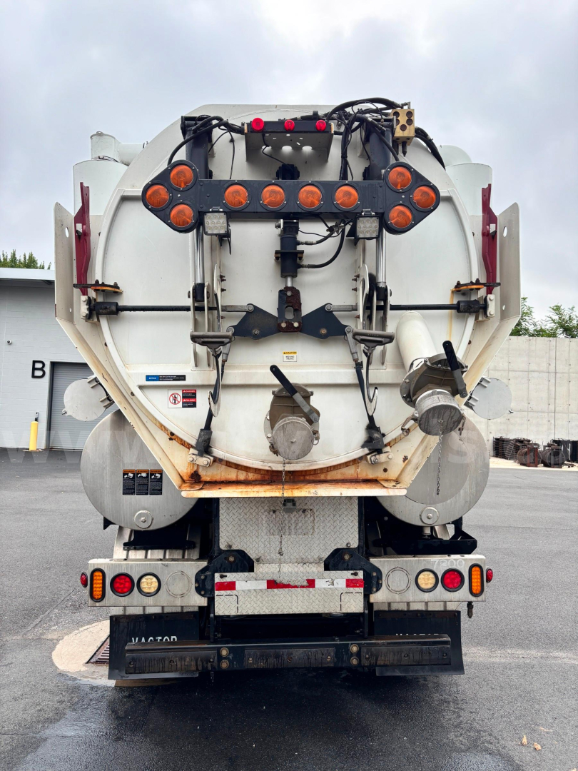 Rear view of a Freightliner vacuum truck with circular rear hoses and taillight assembly. Visible are hoses, hoses connectors, and warning labels.