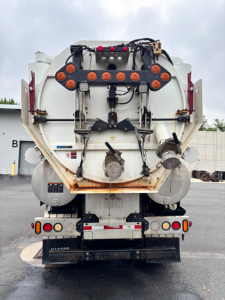 Rear view of a Freightliner vacuum truck with circular rear hoses and taillight assembly. Visible are hoses, hoses connectors, and warning labels.