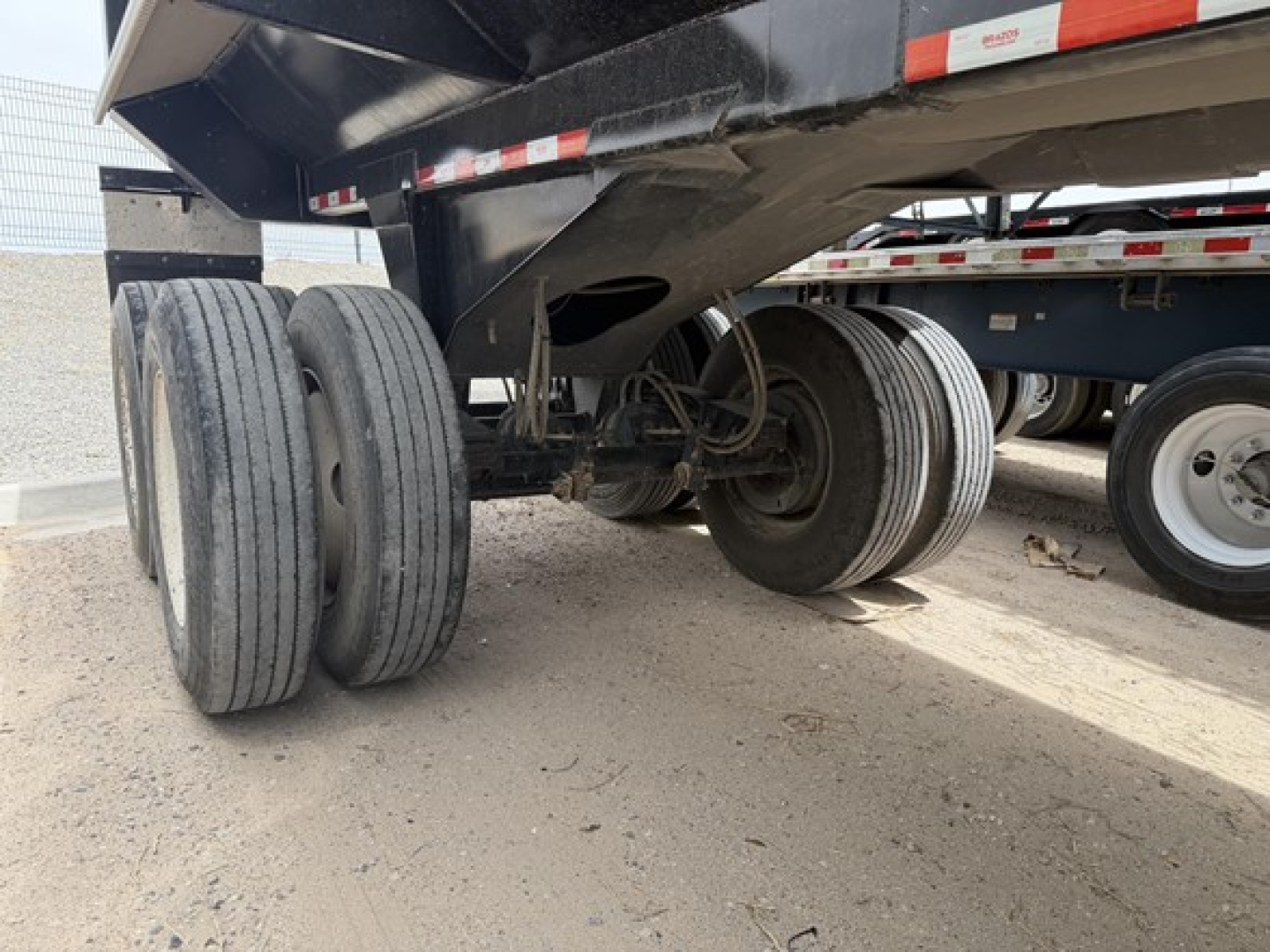 Frameless rock end dump trailer underside showing twin rear axles, suspension and tires, with spare tires nearby.