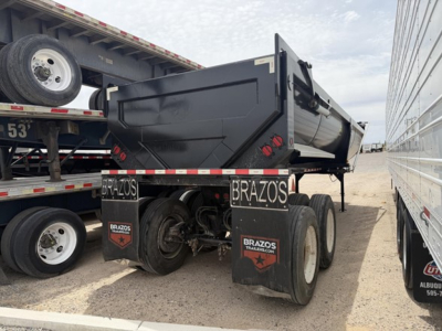 Dump trailer from rear-right angle showing frameless end dump bed with dual rear axles, BRAZOS mudflaps, and black paint.