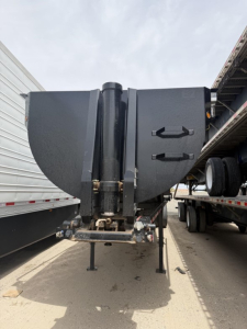 Frameless rock end dump trailer hitch and front-end area with black composite body panels, storage compartments, and landing gear visible.