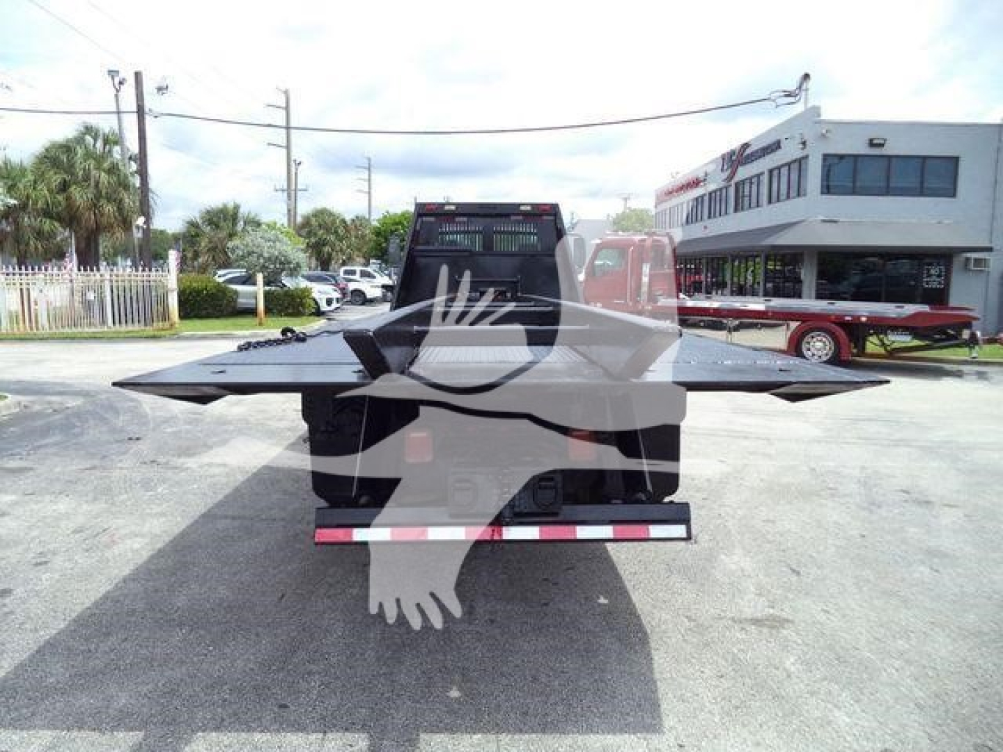 Back view of a 2006 Freightliner M2 106 roll-off truck with a flatbed and rearmost tailgate, visible in a dealership lot.