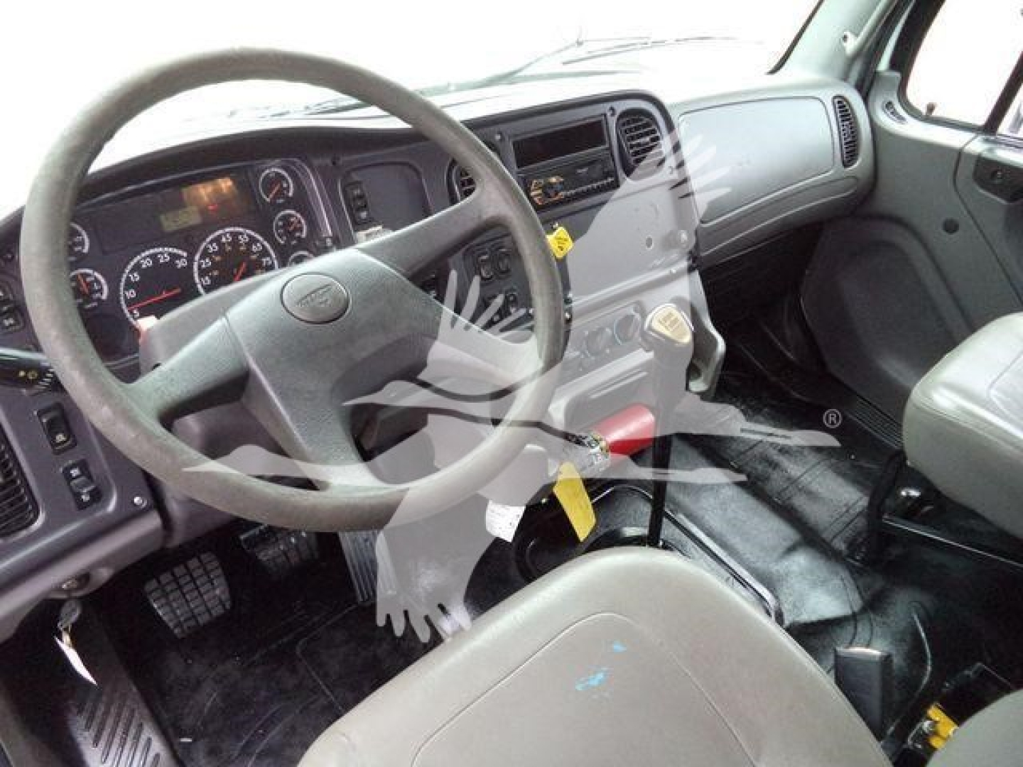 Cab interior of a Freightliner M2 106 truck showing steering wheel, dashboard, and gear shifter.