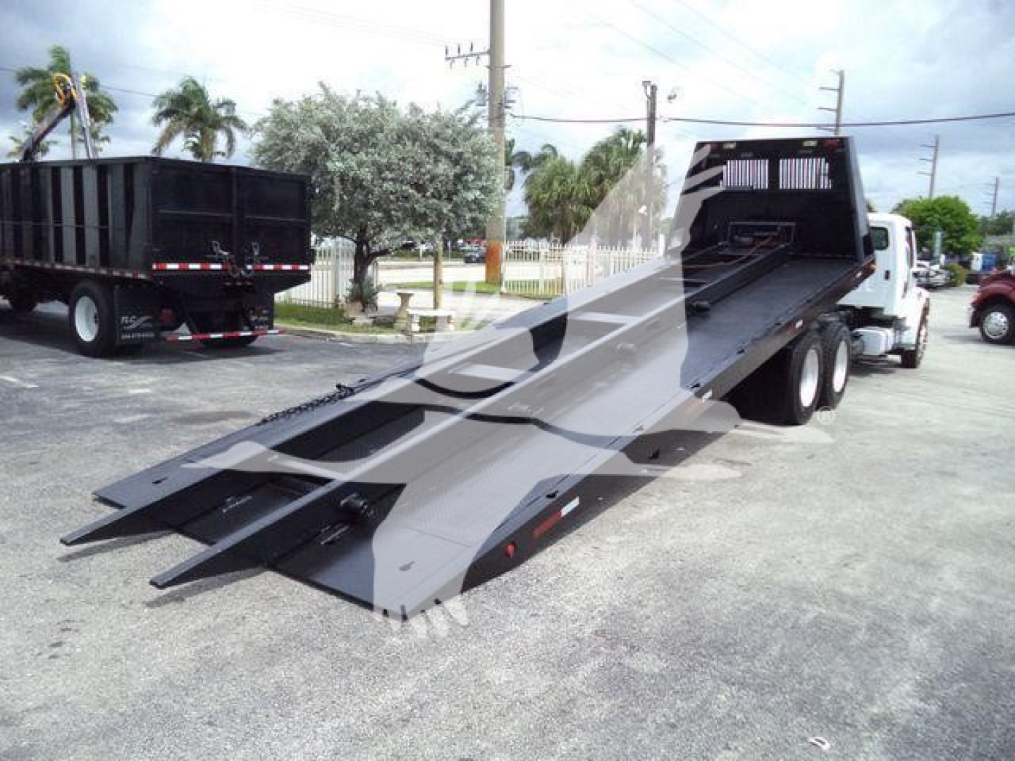 Freightliner M2 106 with a flatbed rollback trailer in lowered position, ramp extensions visible, white cab, black steel bed.