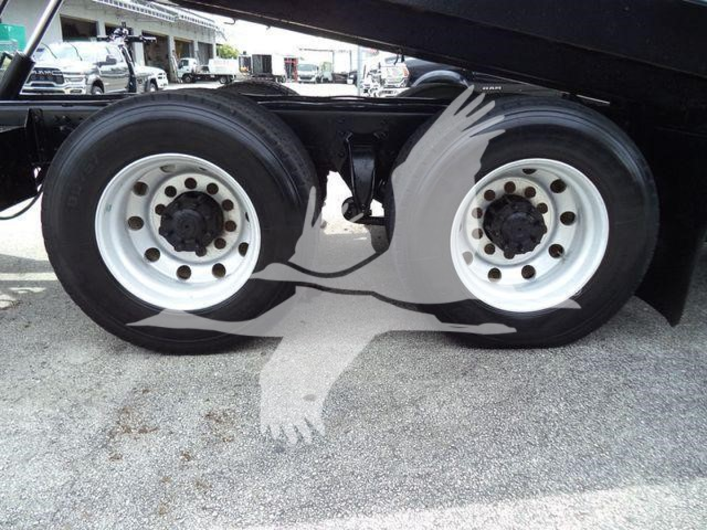 Two rear dual tires of a Freightliner M2 106 roll-off truck showing white wheels and black tires.