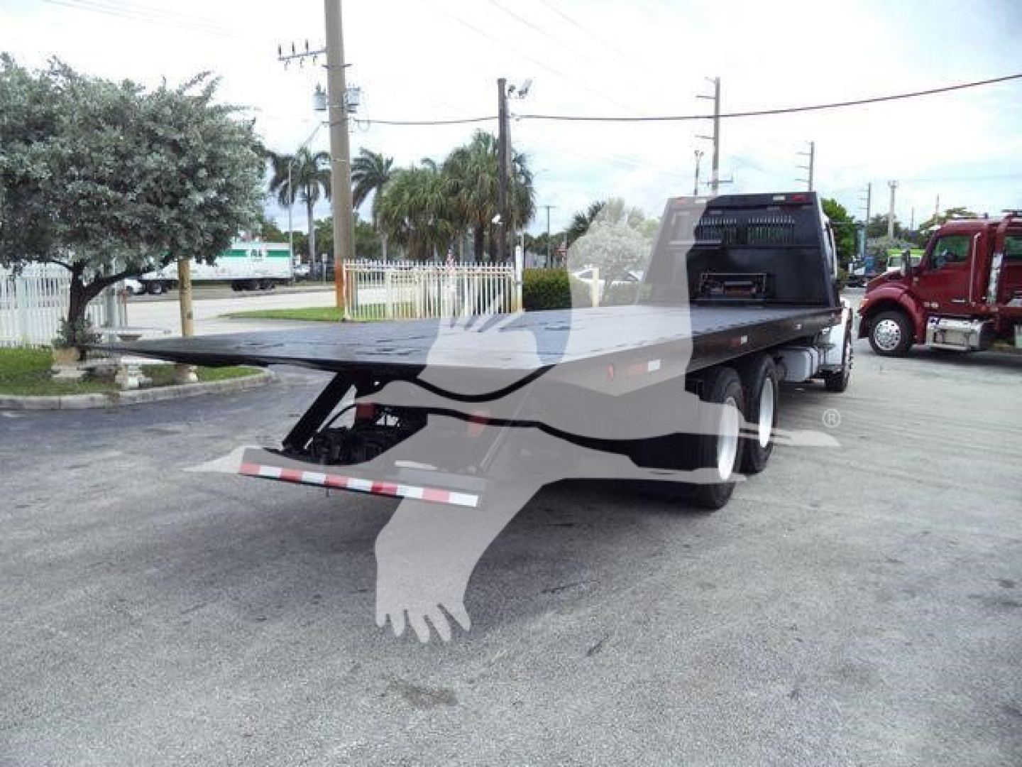 Flatbed rollback truck trailer with rear undercarriage and ramp folded, Freightliner M2 style truck in background.