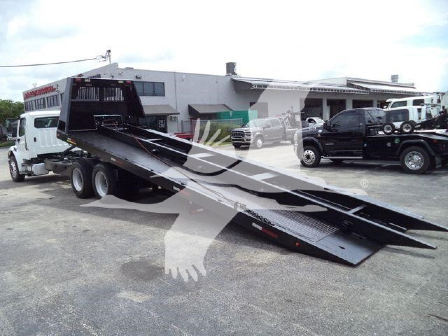 Truck-mounted rolloff with flatbed/boom and loading ramps, Freightliner M2 106 style, two-axle truck with lowered bed for roll-off, visible in yard