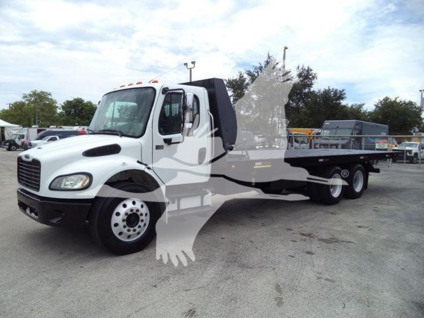 Freightliner M2 106 roll-off truck in a yard, white cab with black trim, dual rear axles, long flatbed/roll-off body, faded canopy area.