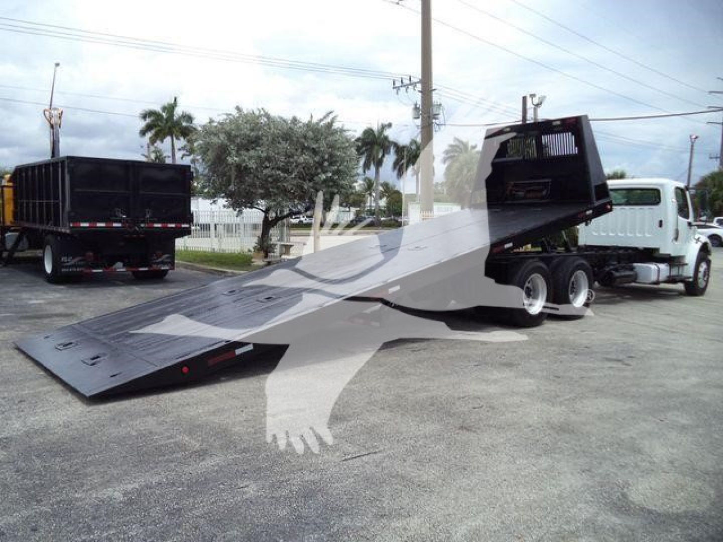 Freightliner M2 106 roll-off truck with tilted loading bed showing hydraulic system and rear cab area