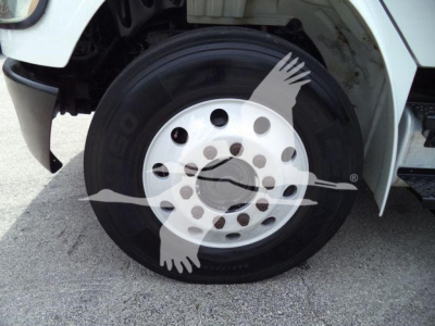 Wheel and tire of Freightliner M2 106 front axle showing steel wheel with multiple lug holes and black tire.