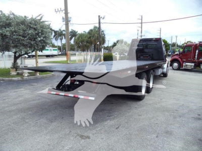 Flatbed rollback truck trailer with rear undercarriage and ramp folded, Freightliner M2 style truck in background.