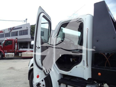 Truck cab interior with open door showing steering wheel and dashboard, Freightliner M2 106 roll-off in background
