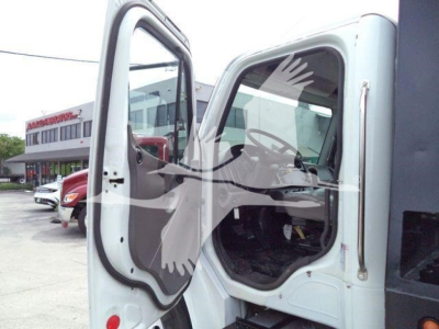 Truck cab interior showing open door of a Freightliner M2 106 rolloff chassis with light gray paint and black interior, background dealership lot.