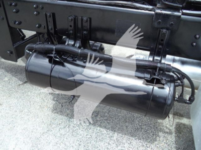 Rolloff truck frame with cylindrical fuel or air tank mounted beneath, visible hoses and mounting brackets.