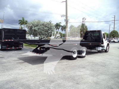 Freightliner M2 106 roll-off truck with long flatbed trailer in a dealership lot showing dual rear axles and hitch.