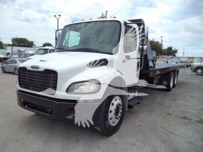 2006 Freightliner M2 106 rolloff truck front-left view with white cab and black grille, rack body on flatbed, stock number 2006M2ROLLOFF visible in a truck lot.