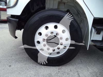 Truck wheel close-up showing front wheel with large hub and black tire on Freightliner M2 106 roll-off truck, part of fender and chassis visible.