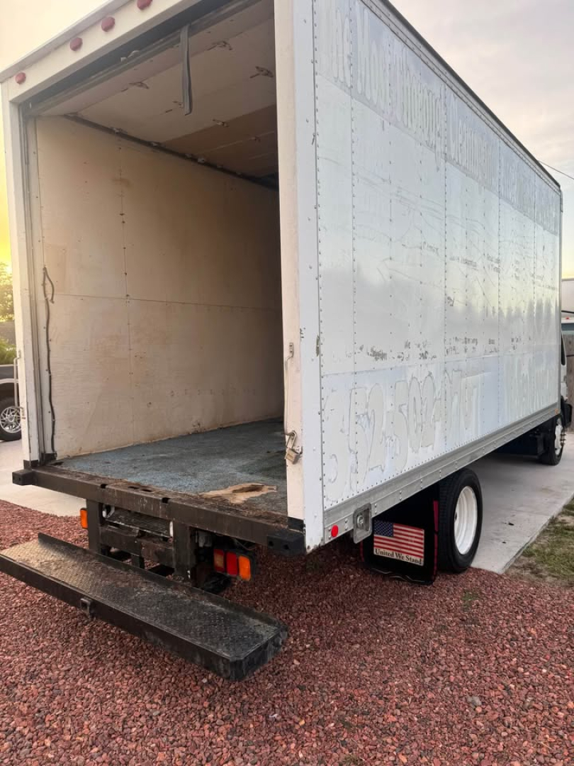 Box truck cargo area of a 2006 International CF500 with rear ramp lowered, empty interior, white exterior panels, and dual rear wheels.