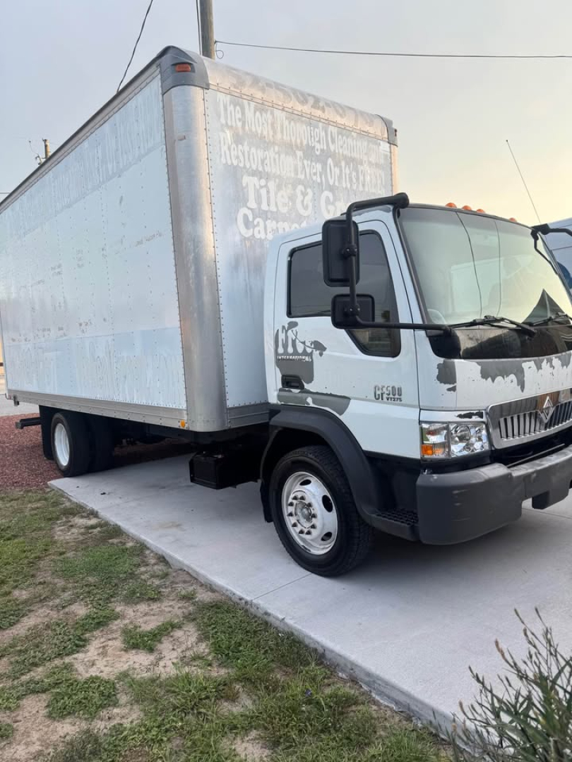 Box truck showing cargo area and cab; CF500 badge visible on front. Side of box has faded painted text; front bumper and wheel well visible.