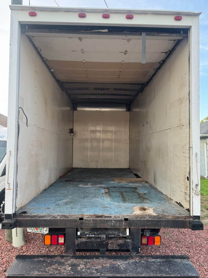 Box truck cargo area with empty interior and rear doors open, showing light-colored walls and floor.