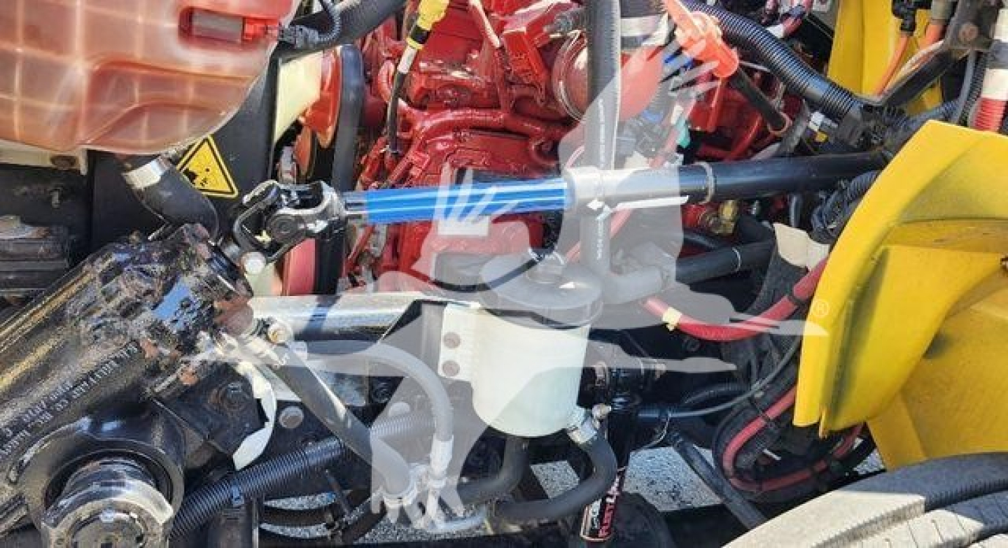 Engine bay of a 2021 International MV truck with red engine components and yellow body parts, showing hoses, belts, and wiring harnesses.