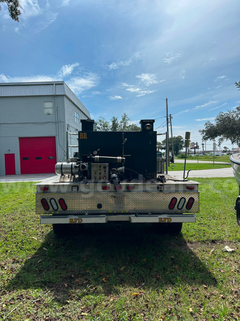 Rear view of a 2011 Ford F-550 service/utility truck with a large black on-board compressor/pump unit mounted on flatbed; visible reflectors, bumper, and license plate area.