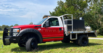 Ford F-550 service/trades truck with red cab and white utility bed, front grille guard, and flatbed toolbox.
