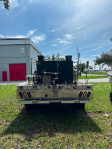 Rear view of a 2011 Ford F-550 service/utility truck with a large black on-board compressor/pump unit mounted on flatbed; visible reflectors, bumper, and license plate area.