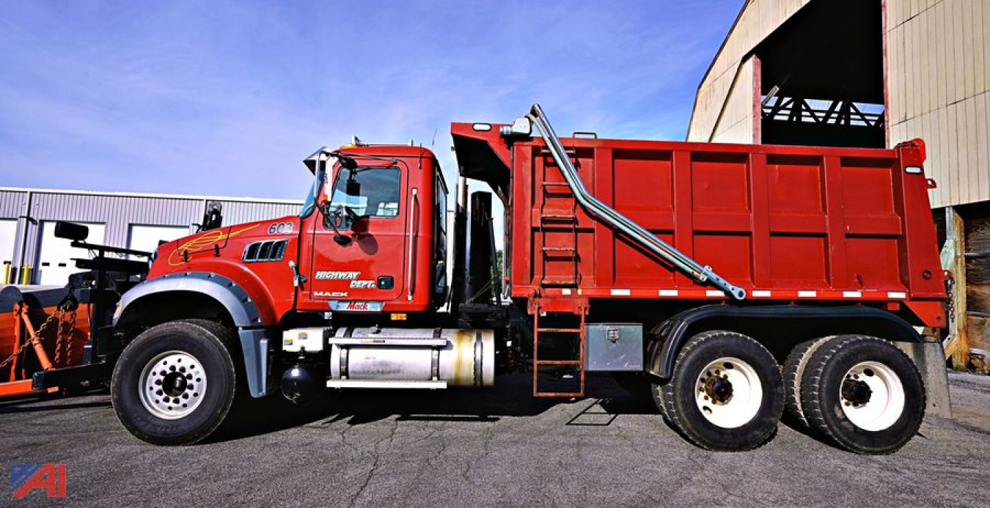 2009 Mack GU713 Granite dump truck with plow and spreader, red cab and dump body, side view showing dual rear wheels and equipment mounts.