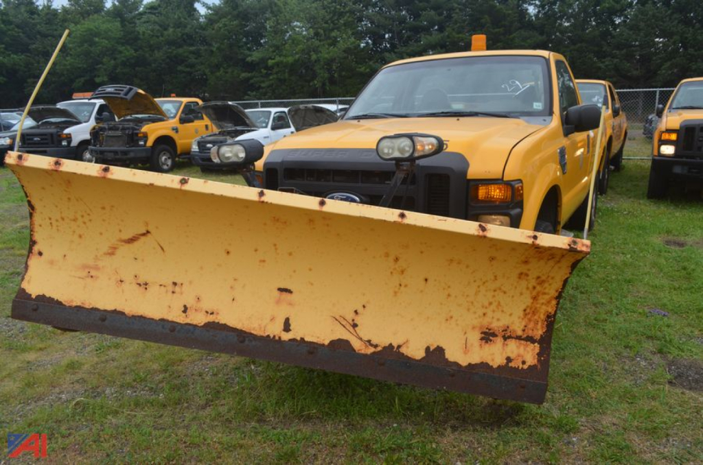 Ford F-250 Super Duty pickup with a large yellow snow plow attached in front, truck in a line of vehicles.
