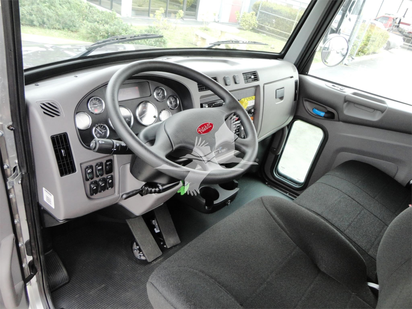 Truck cab interior of a 2022 Peterbilt 337, dashboard with gauges, steering wheel, pedals, and driver's seat visible.