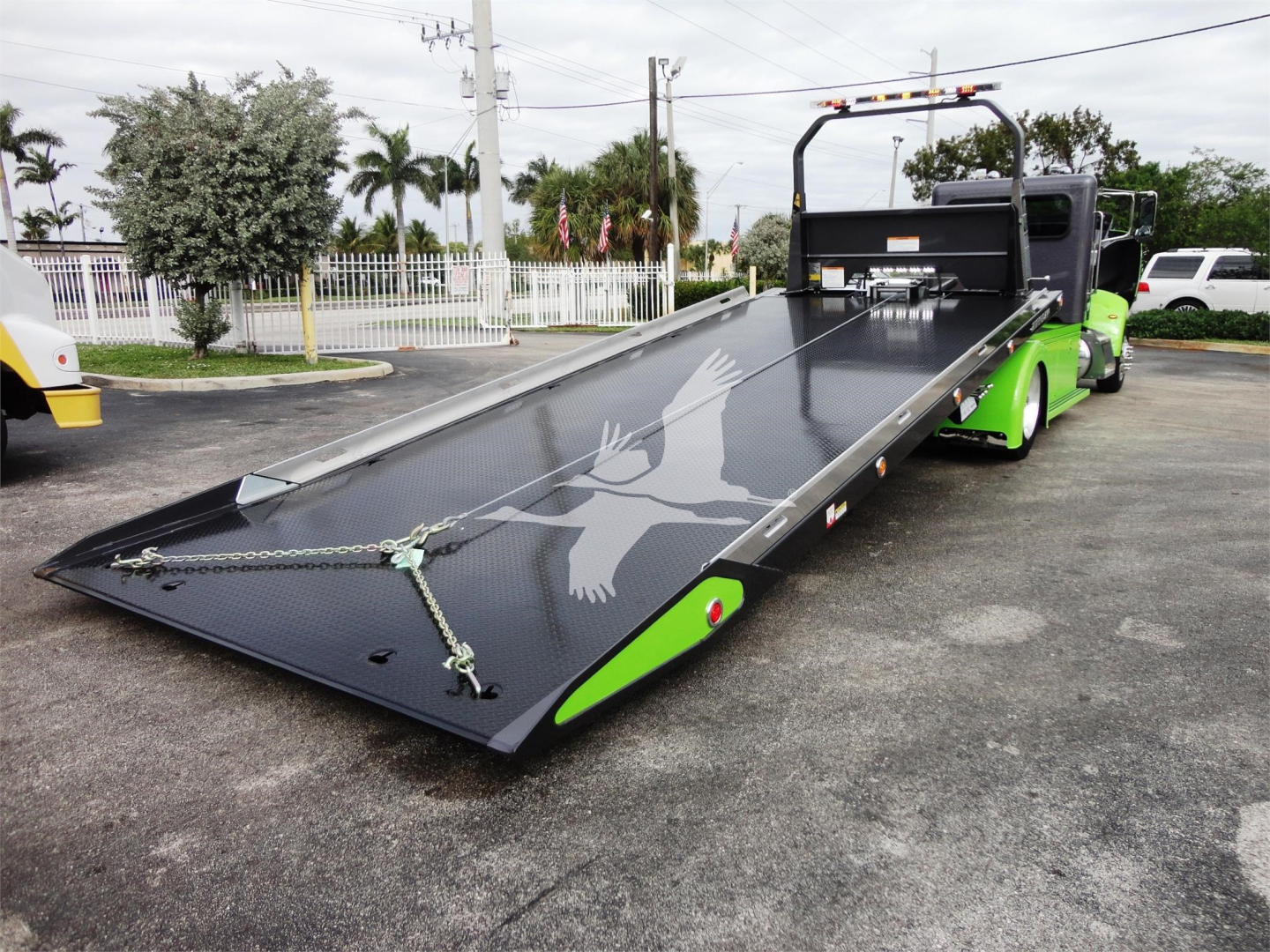 2022 Peterbilt 337 rollback truck with a long flatbed in a parking lot, green accents on the cab, and a winch at the rear