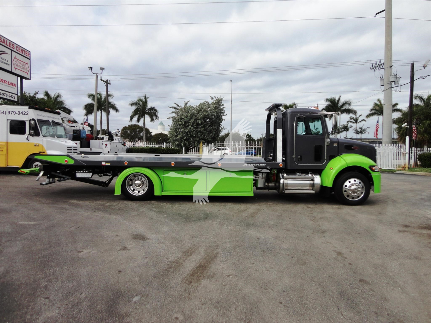 Side view of a 2022 Peterbilt 337 rollback tow truck with bright green and black color scheme and a long flatbed.