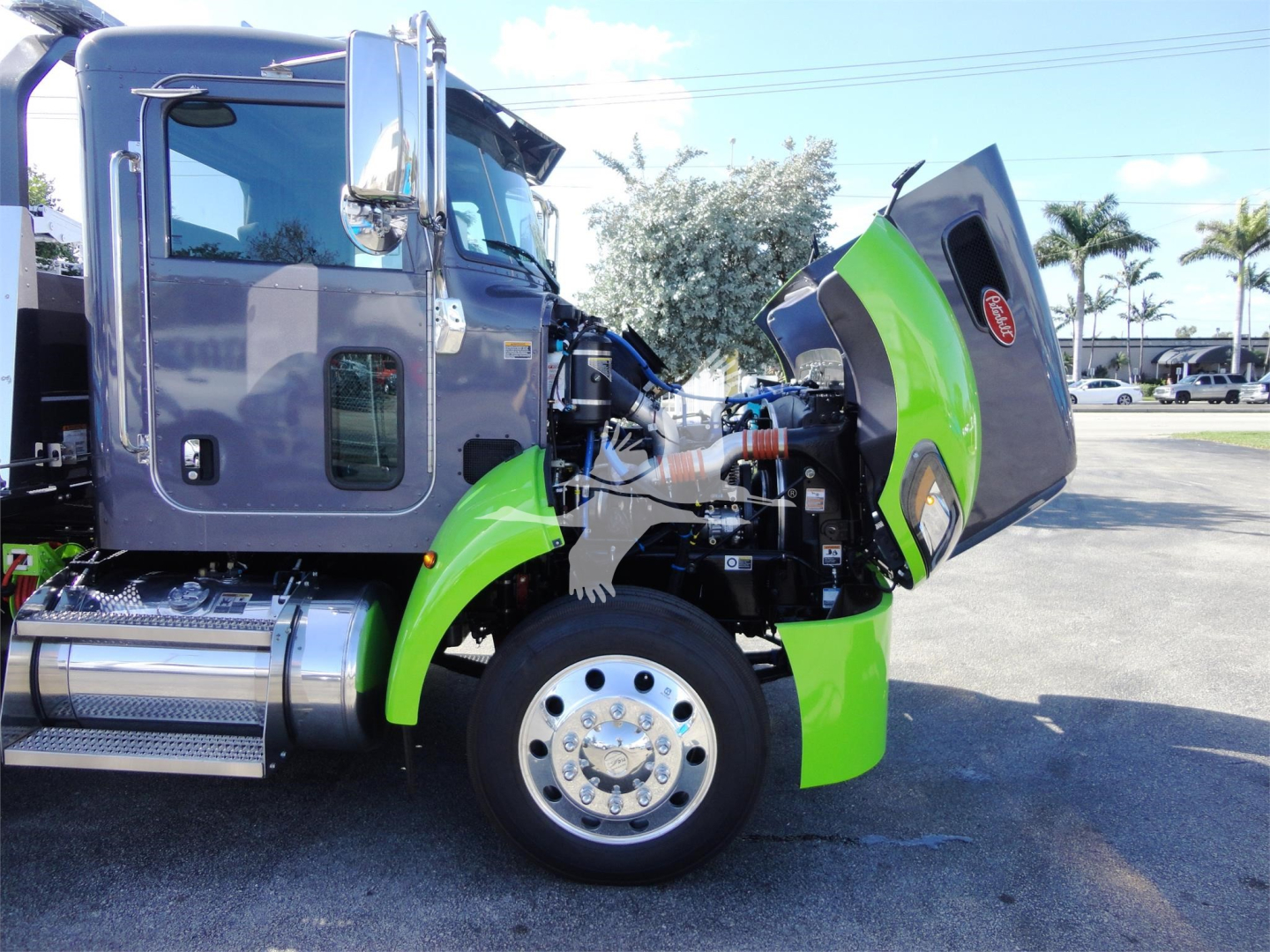Truck engine bay showing green Peterbilt 337 with hood open and front wheel visible