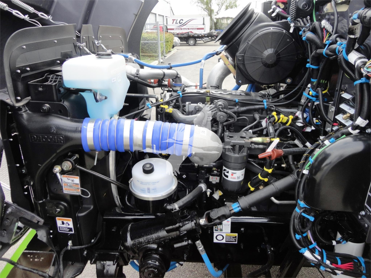 Peterbilt 337 engine bay view with blue coolant reservoir, white expansion tank, and wiring harnesses.