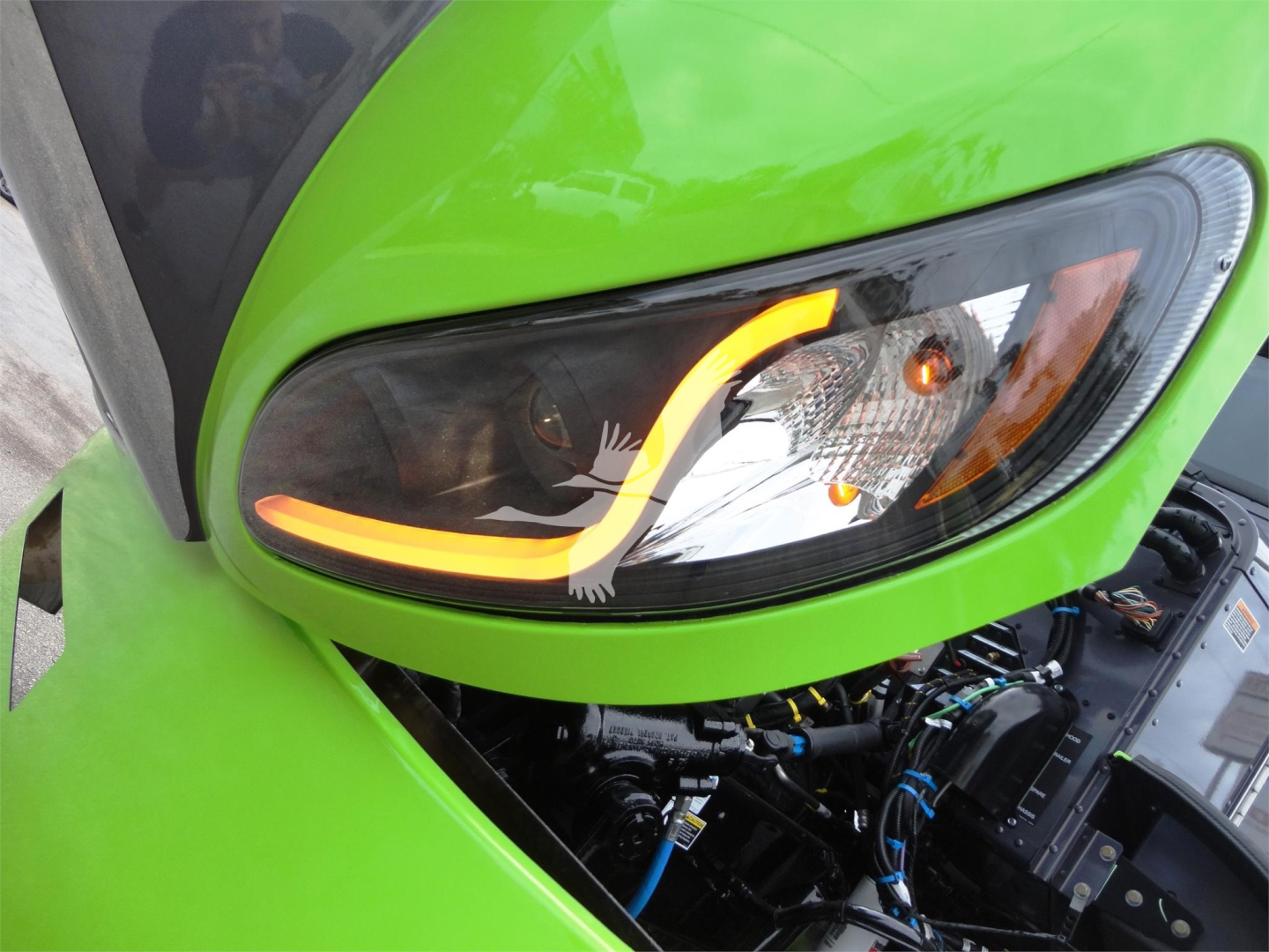 Front left headlight area of a bright green Peterbilt 337 truck showing engine bay with wiring and components visible