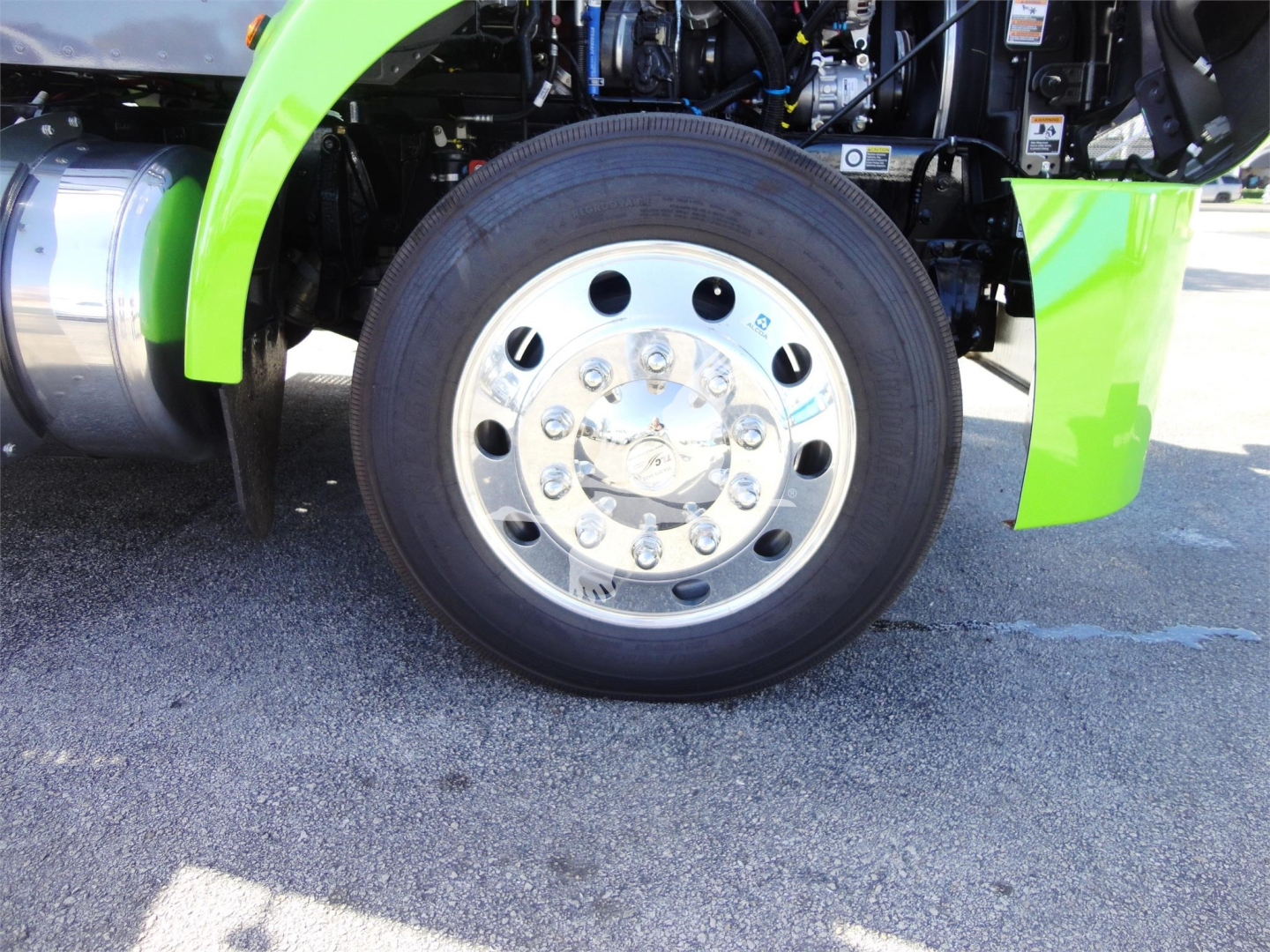 Peterbilt 337 front wheel and green fender showing chrome wheel with multiple lug nuts and tire, engine bay area visible.