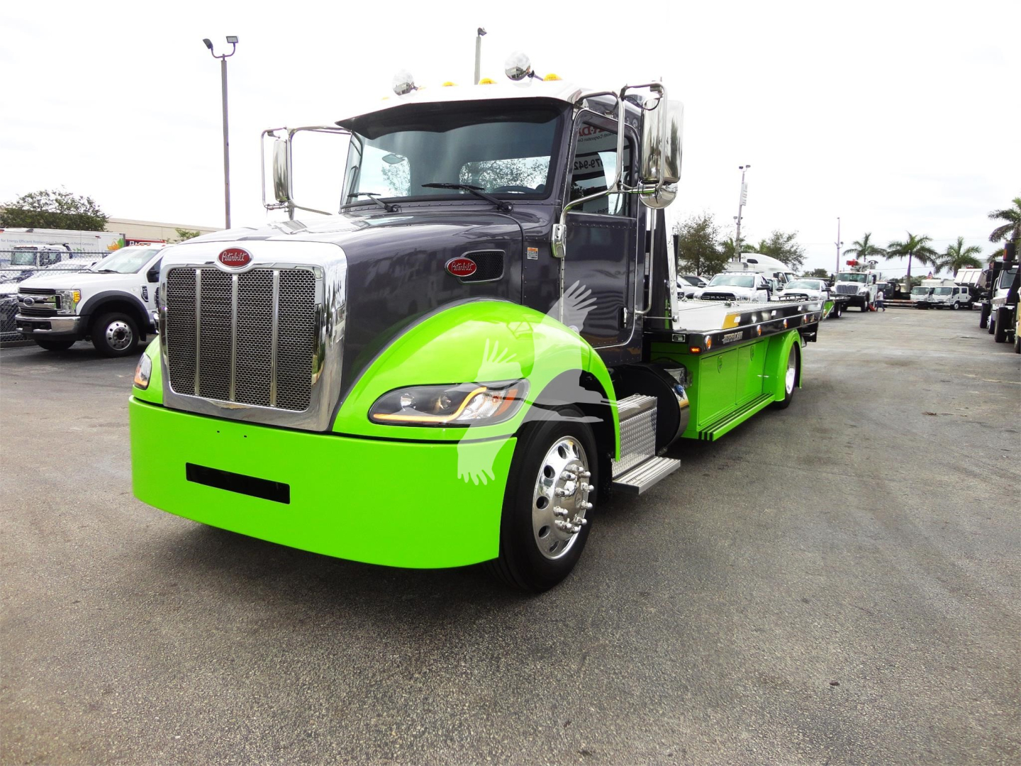 Peterbilt 337 rollback tow truck with bright green lower body and black cab, chrome grille, and side mirrors. Stock number J56626 visible in a vehicle lot.