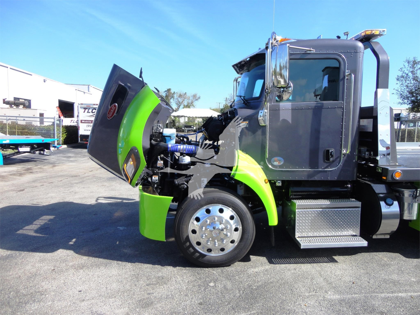 Peterbilt 337 rollback truck with hood open, showing green accent panels and chrome wheel, cab door visible, engine bay exposed.