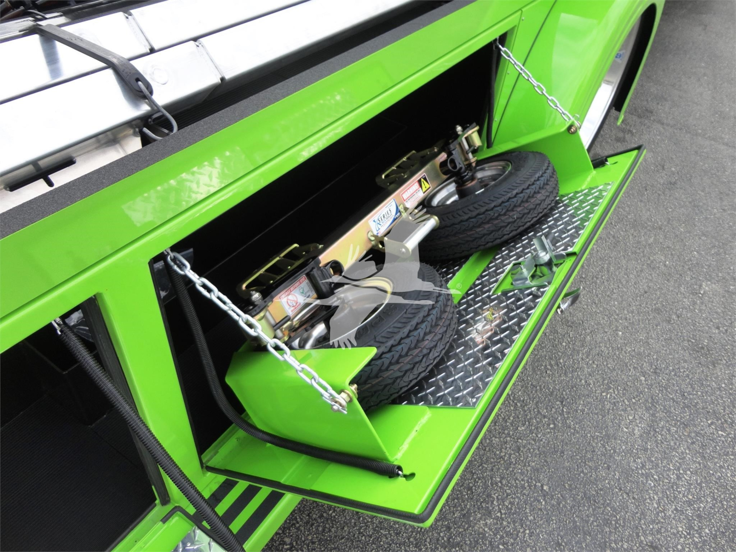Green Peterbilt 337 rollback truck rear storage compartment with mounted spare tires and chain latches visible.