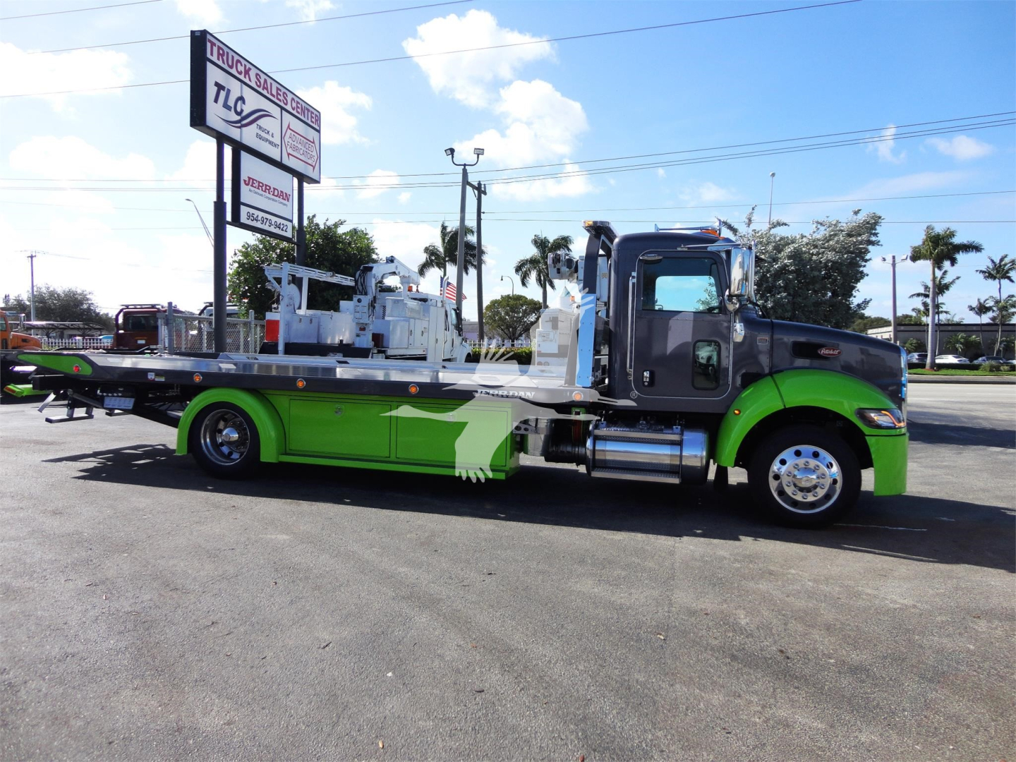 Peterbilt 337 rollback truck with a lime green and black color scheme, long flatbed, chrome exhaust stacks, and heavy-duty tow equipment in a dealership lot.