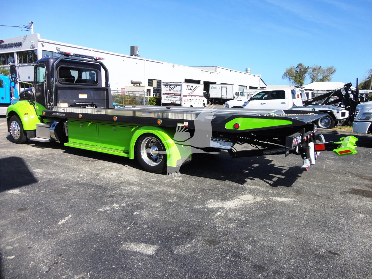 Peterbilt 337 rollback tow truck in lime green and black, side view with flatbed, branding and equipment visible in a lot.