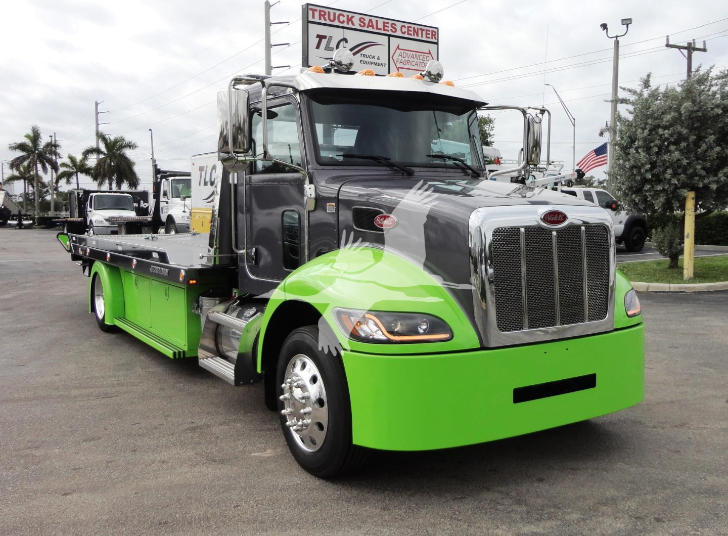 Peterbilt 337 rollback tow truck in green and gray color with chrome grille, visible cab and flatbed section.