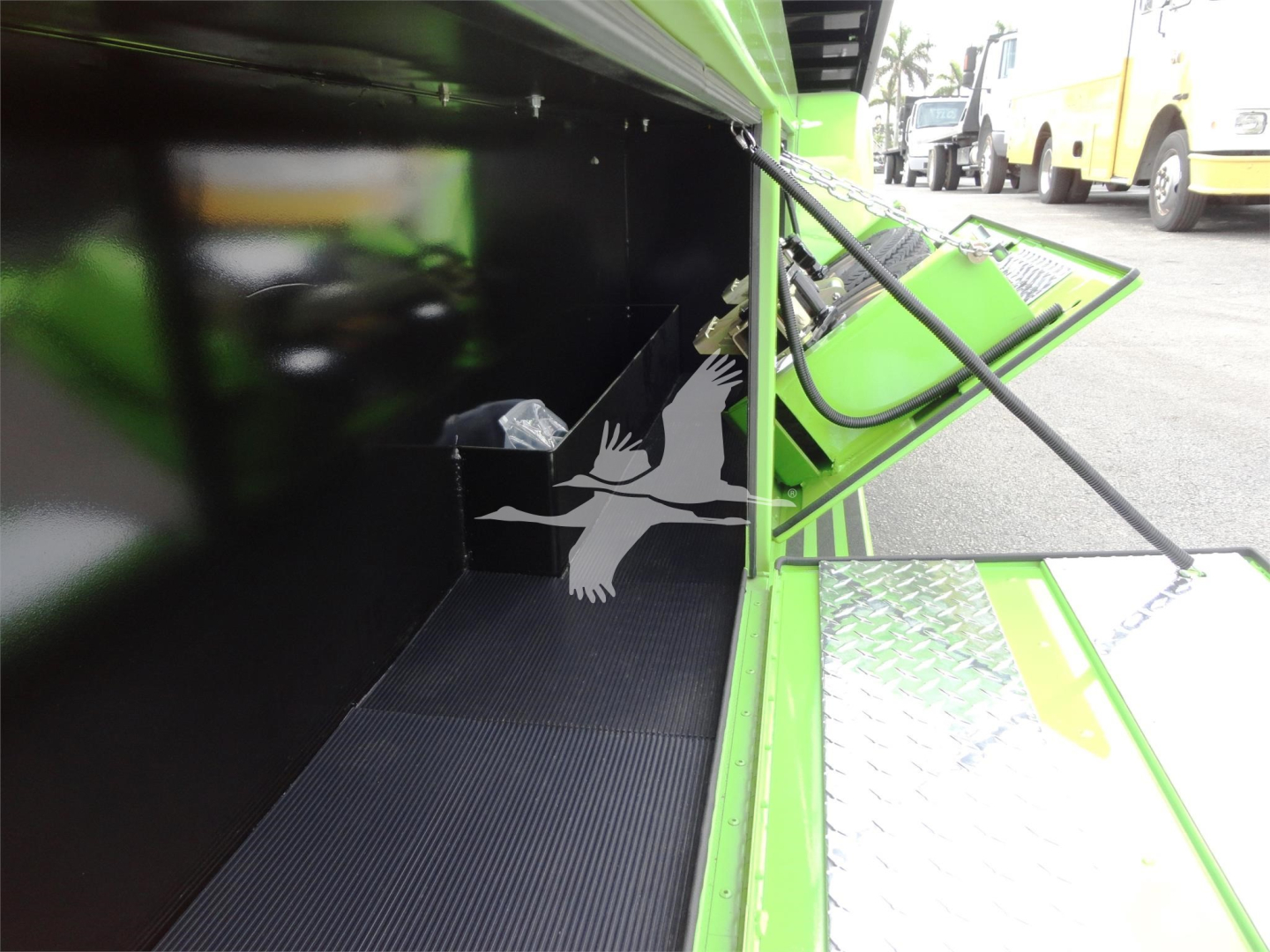 Truck bed area inside a green Peterbilt rollback unit showing a black interior panel and a small storage compartment with a plastic bag.